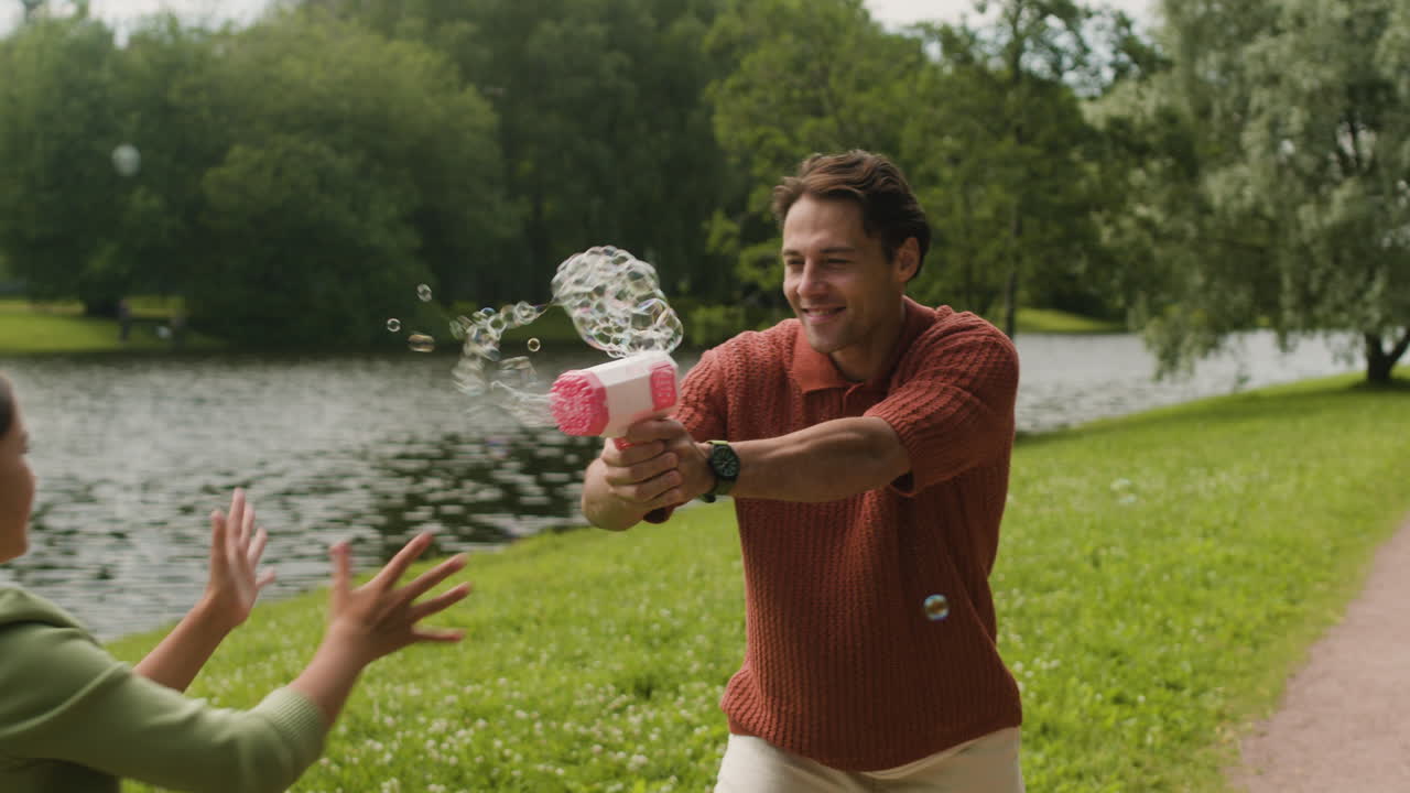 Man and girl playing with bubble gun in park