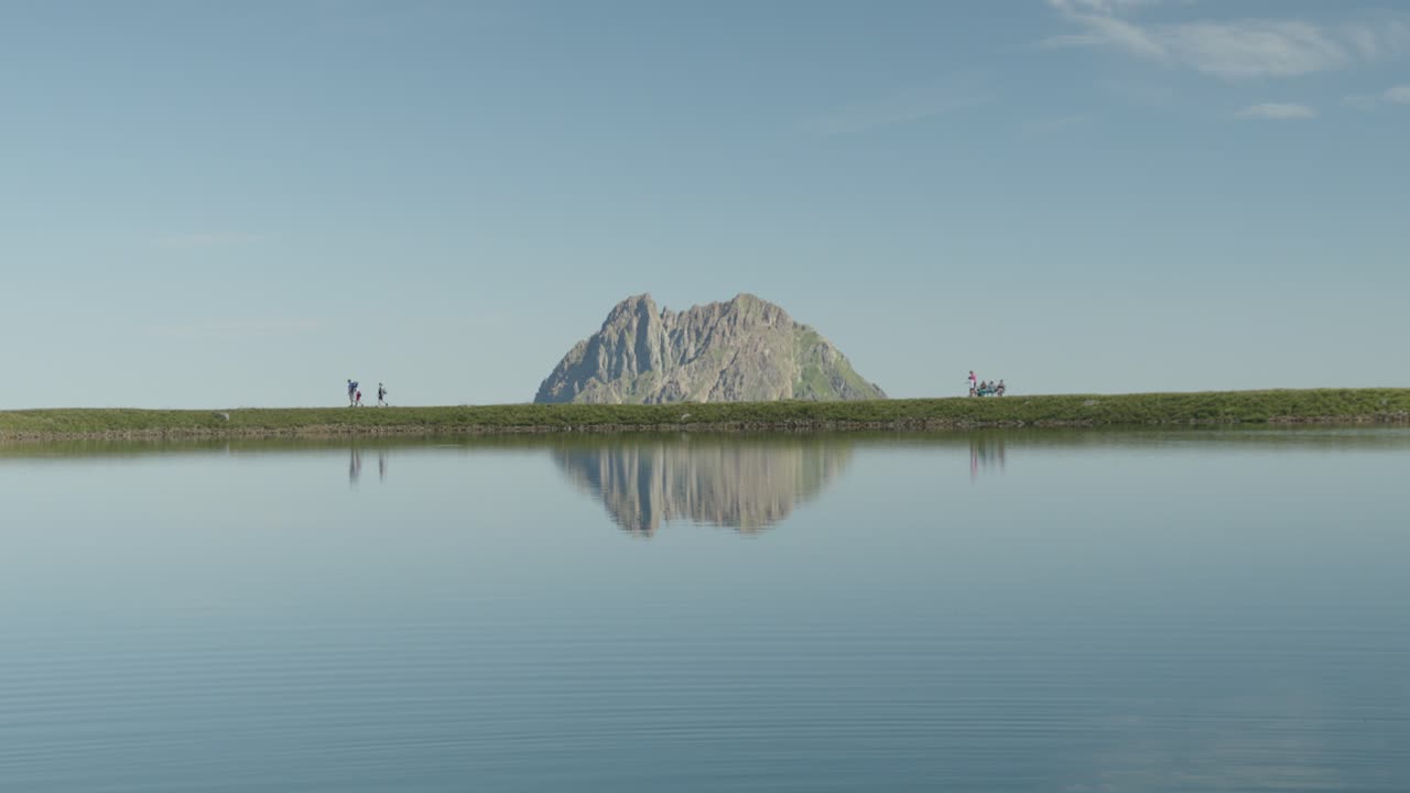 은 호수, 웅장한 산의 배경, 그리고 해변을 따라 산책하는 사람들