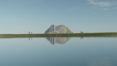 a clear lake, a majestic mountain backdrop, and hikers along the shore