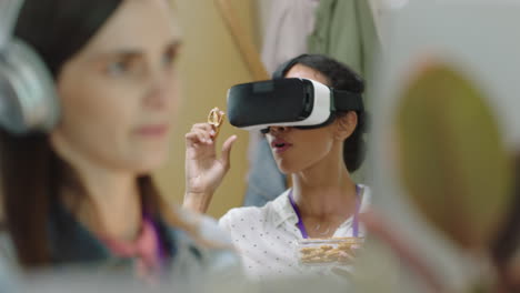 Feliz-Mujer-De-Negocios-Con-Auriculares-De-Realidad-Virtual-Disfrutando-Del-Entretenimiento-Durante-El-Almuerzo-Comiendo-Pretzels-En-Un-Colorido-Y-Moderno-Lugar-De-Trabajo-De-Oficina