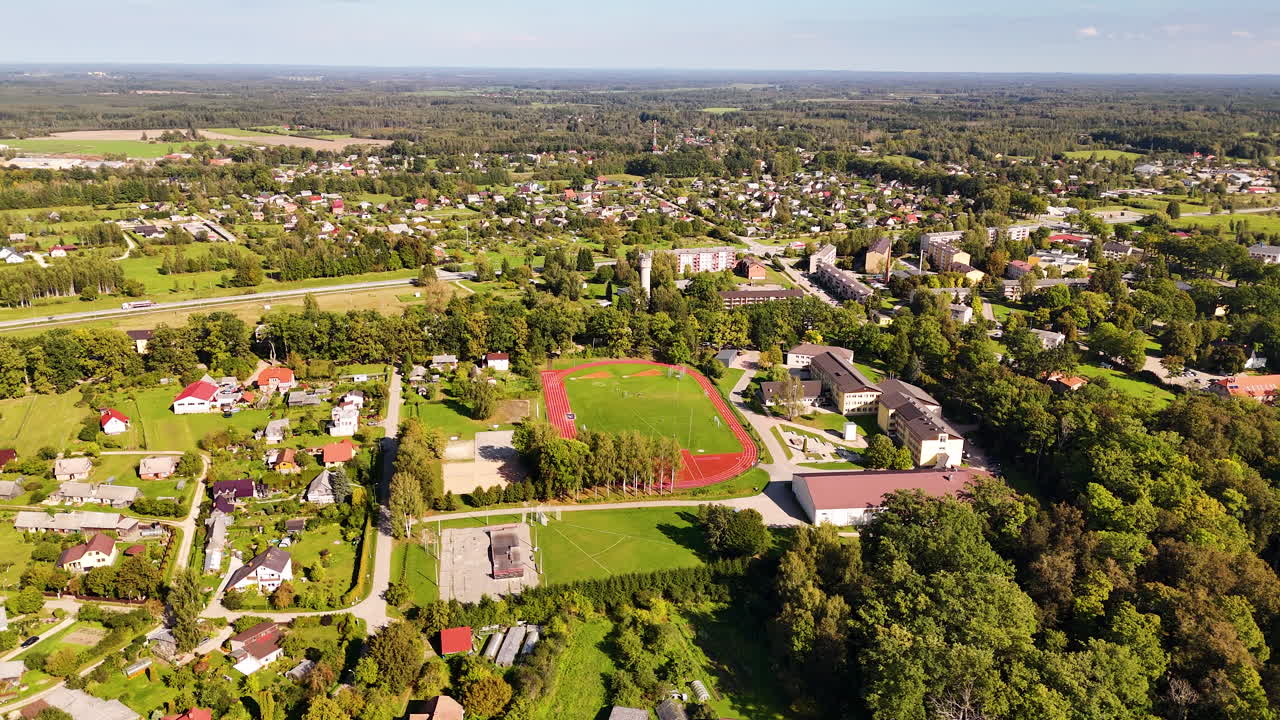 Drone view of Koknese, Latvia, featuring a red running track and buildings amid greenery.