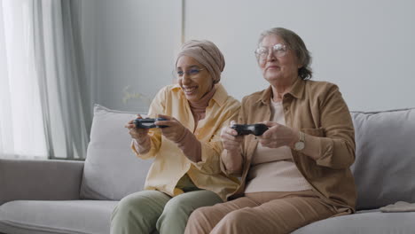 Glückliche-Arabische-Frau-Mittleren-Alters-Und-ältere-Dame,-Die-Zusammen-Videospiel-Spielen-Und-Spaß-Haben,-Während-Sie-Zu-Hause-Auf-Dem-Sofa-Sitzen