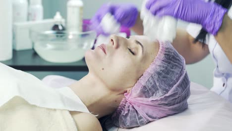 Process of removal a cosmetic cream from the face of a young woman with napkins in spa salon. Hands of the cosmetologist in gloves cleaning face. Facial skin care.