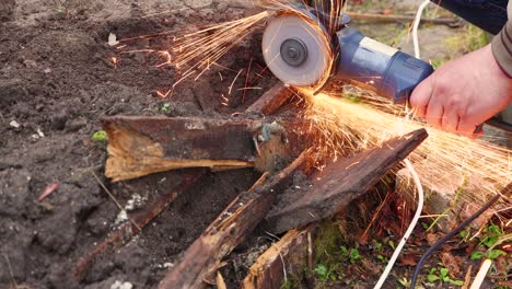 Close-up male hands with an angle grinder cut a rusty metal greenhouse.