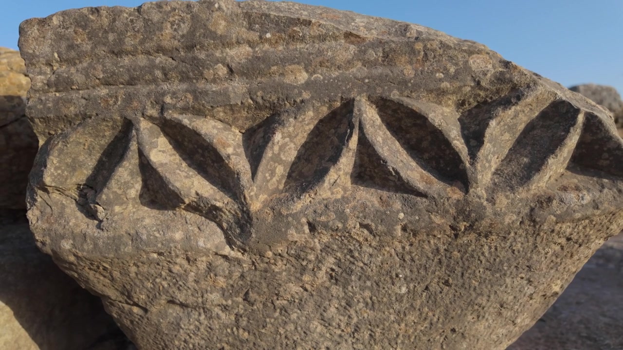 Vue cinématographique rapprochée d'un ornement en pierre sculptée de la Rome antique sur le site archéologique de Volubilis, classé à l'UNESCO, soulignant l'artisanat classique préservé au Maroc romain.