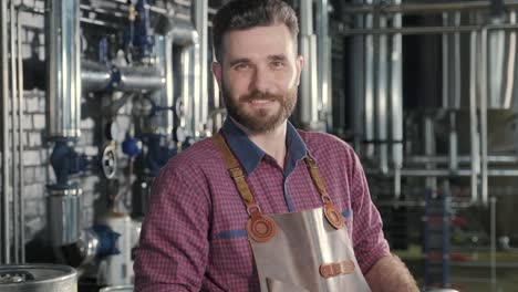 young brewer wearing a leather apron carries a barrel of craft beer at a modern brewery