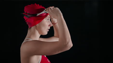 una nadadora con un traje de baño rojo y una gorra, preparándose para competir en una piscina.