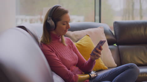 woman with prosthetic with wireless headphones listening to music on mobile phone on sofa