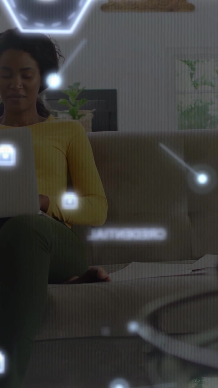 Vertical video: Woman working on laptop at home, typing and causing tech HUD hex dots drifting