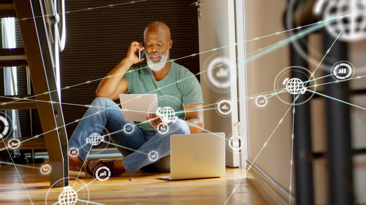 Holding phone, paper, man wearing teal tee sitting in doorway hardwood-floor, laptop network moving