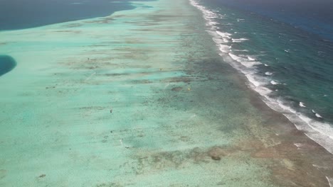 Kitesurfers-gliding-over-the-clear-blue-waters-of-los-roques-barrier-reef,-aerial-view