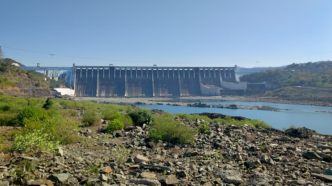 Barragem de Sardar Sarovar no Rio Narmada perto da Estátua da Unidade, Kevadia, Gujarat, Índia. Enorme barragem de concreto com rio a fluir, margem rochosa e colinas. Grande projeto hidrelétrico e popular destino indiano.