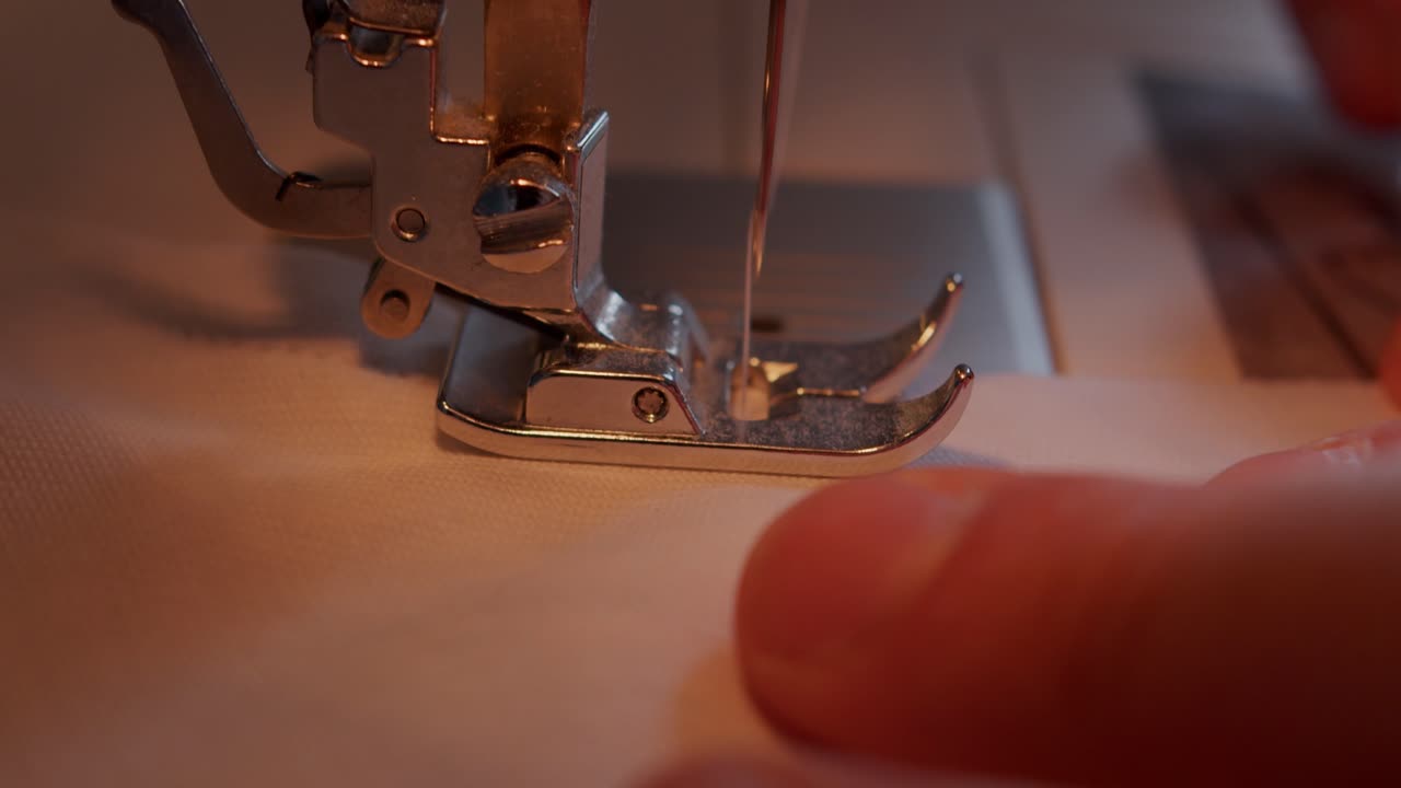작업자의 손에 의해 이동된 천으로 재봉틀 발을 통해 이동하는 바늘의 가까운 측면 보기