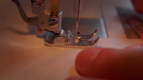 vista lateral cercana de la aguja moviéndose a través del pie de la máquina de coser hacia la tela movida por las manos del operador