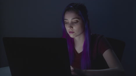 niña trabajando en su computadora portátil, la habitación está oscura y la pantalla ilumina su cara