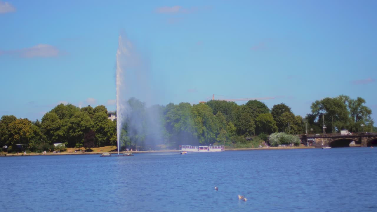 4K Slow Motion Shot of a giant water fountain in a lake in Hamburg, Germany. A boat swims through the water.