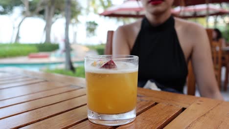 person sipping a cocktail at a wooden table.