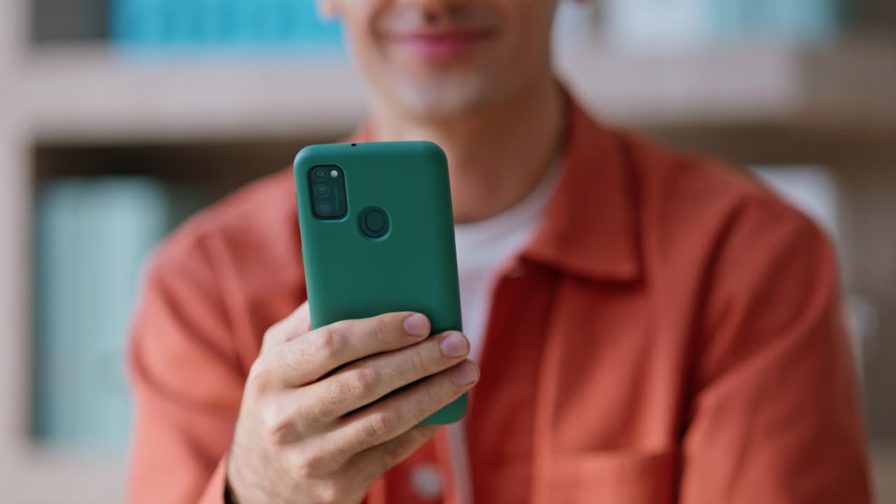 Smiling guy watching social media on cellphone sitting apartment home closeup