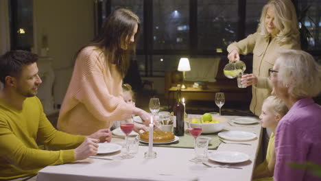 mujer cortando pastel durante una cena con su familia feliz