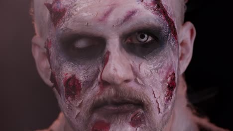 frightening man with halloween zombie makeup blows smoke from nose and mouth, trying to scare