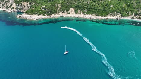 Un-Velero-En-Las-Vívidas-Aguas-Azules-Cerca-De-La-Isla-De-Corfú,-Grecia,-Senderos-En-El-Mar,-Vista-Aérea