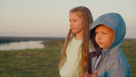 dos niños pequeños, una niña y un niño, de pie juntos en un campo y mirando la puesta de sol.