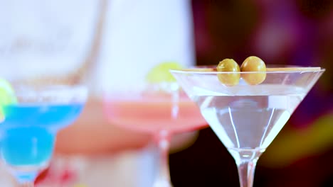 vibrant cocktails in various glasses with olives and lime garnishes, set against a blurred background, showcasing a lively atmosphere