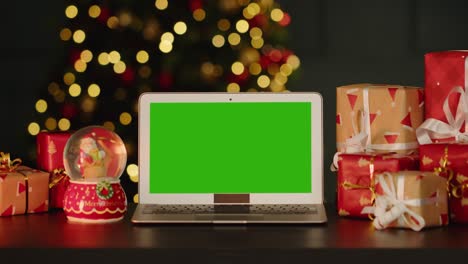 portátil con pantalla verde en la mesa con decoraciones de navidad contra el árbol de navidad