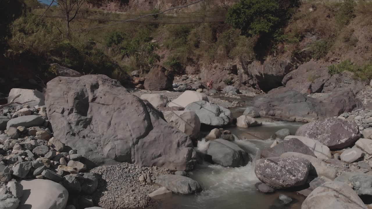 rocky river winding through mountains in canyon valley water flowing approaching grey boulders green trees slow aerial smooth moving forward proximity to rocks cascading water creek