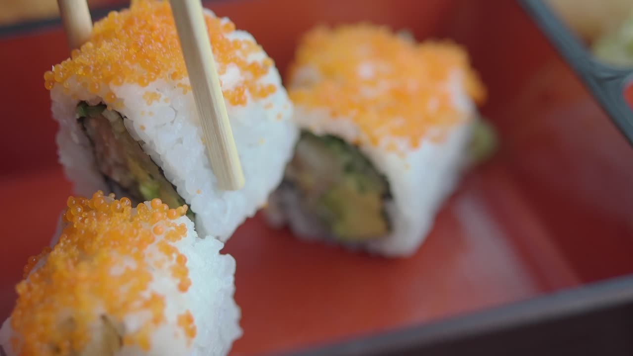 Bacchette che prendono un fresco roll di sushi California da un piatto rosso.