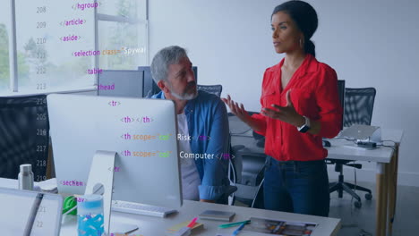 woman presenting code review to colleague in open-plan office, showing animated html snippets