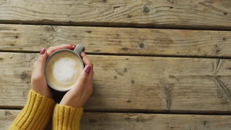 video of hands of caucasian woman holding mug with coffee on wooden surface