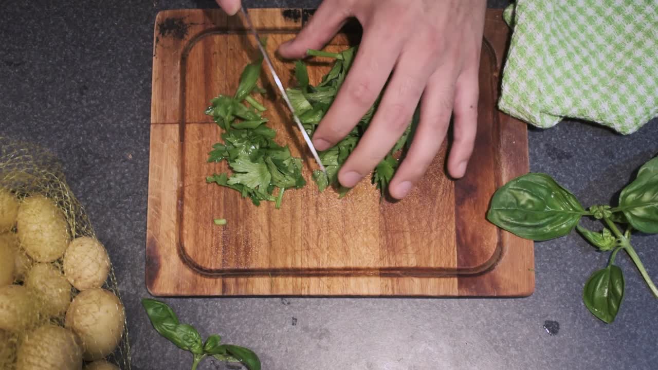 Young male cutting celery in his kitchen on top of a cutting board with a sharp knife