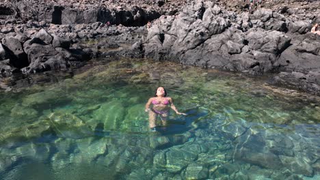 the aerial perspective reveals a radiant woman in a swimsuit resting on the sea, relishing her time away