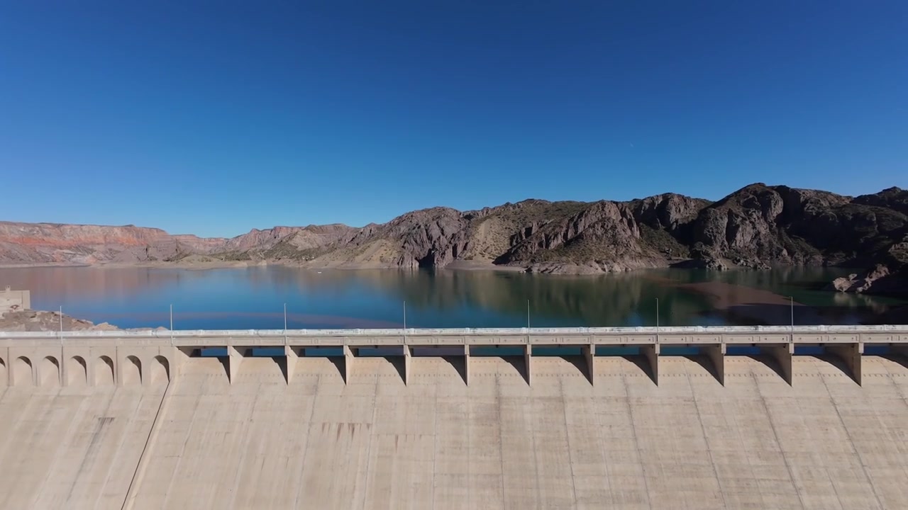 Aerial view of large concrete dam, turquoise reservoir, and arid canyon landscape