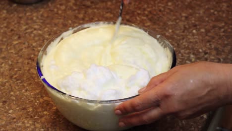 Slowly-mixing-whipped-egg-yolk-and-white-for-baking-a-sponge-cake-in-a-glass-bowl