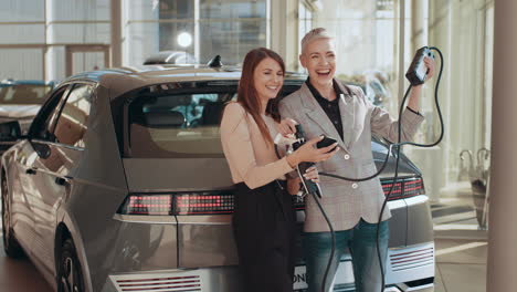 dos mujeres cargando un coche eléctrico en una sala de exhibición