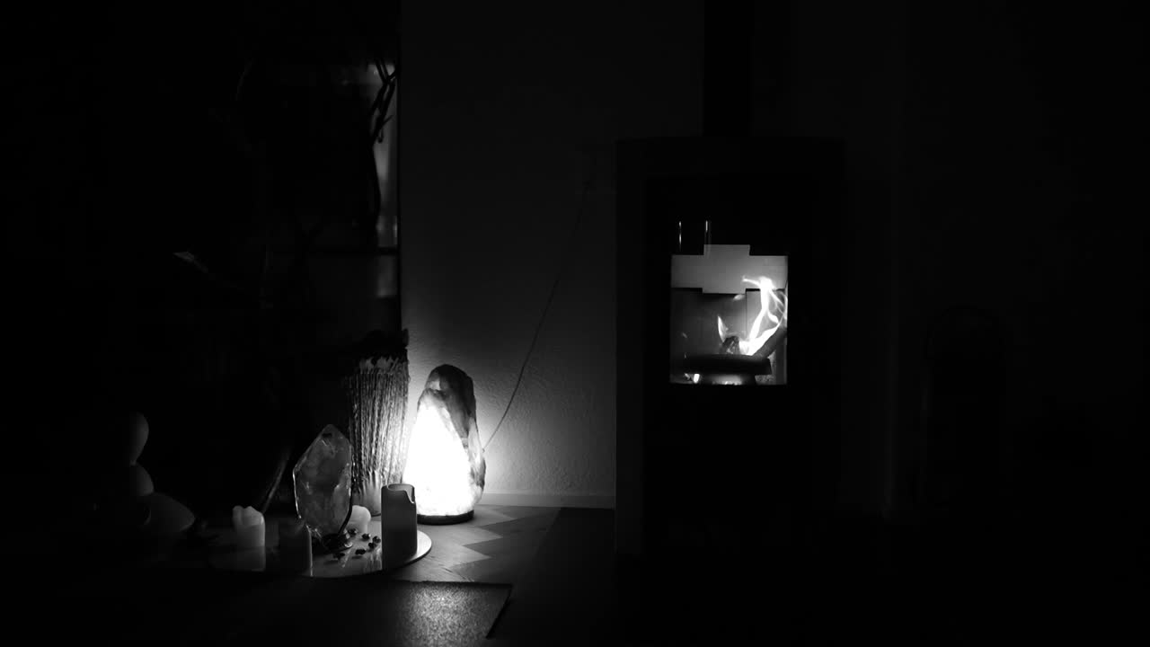 Black and white view of firewood crackling inside home fireplace with flickering flames in slow motion, glowing embers and soothing warmth, peaceful atmosphere.