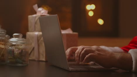 santa's hands are typing on a laptop keyboard. santa claus is distributing gifts for good children for christmas and new year.