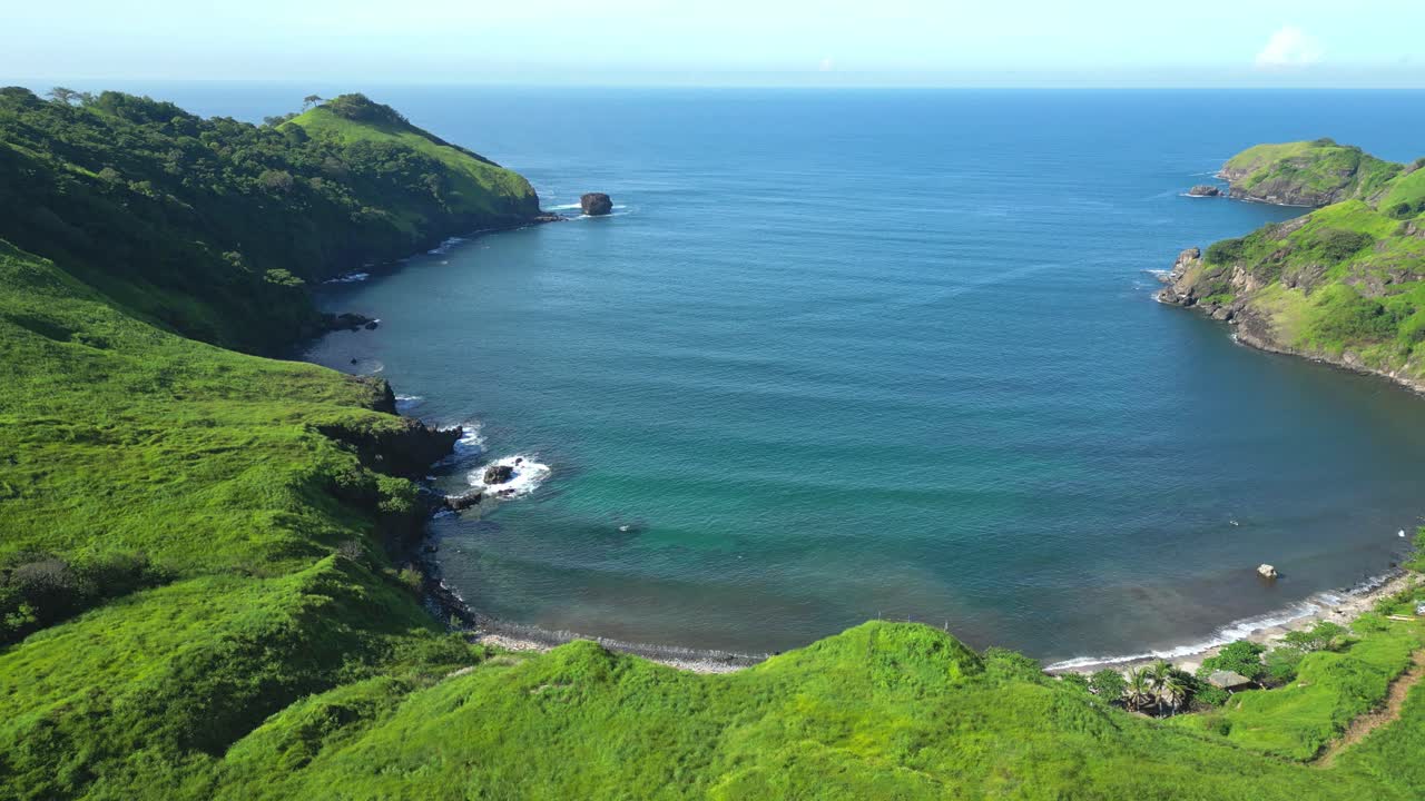 Tilt‑down aerial of Nagbayog View Deck in Mariveles, Bataan, revealing the curved coastline as lush green hills descend into turquoise waters under soft natural light