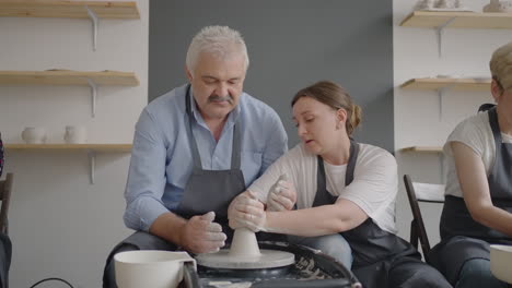 una mujer maestra comparte sus habilidades con un hombre mayor dirigiendo una lección para los ancianos. muestre al abuelo la técnica de trabajar en una rueda de alfarero con arcilla cerámica