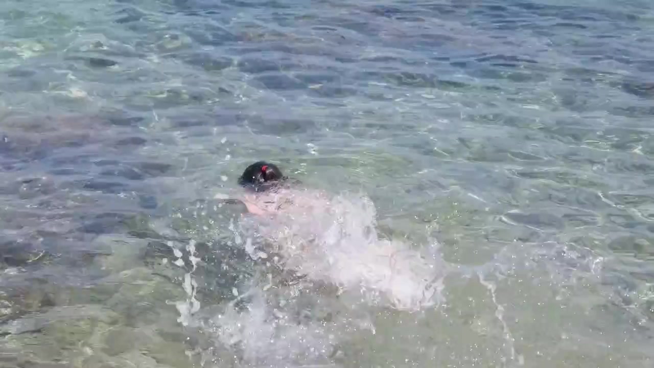 Primo piano di un bambino che nuota in acque basse e limpide vicino a rocce, schizzando sotto il sole, Isola di Santa Margherita, Francia.