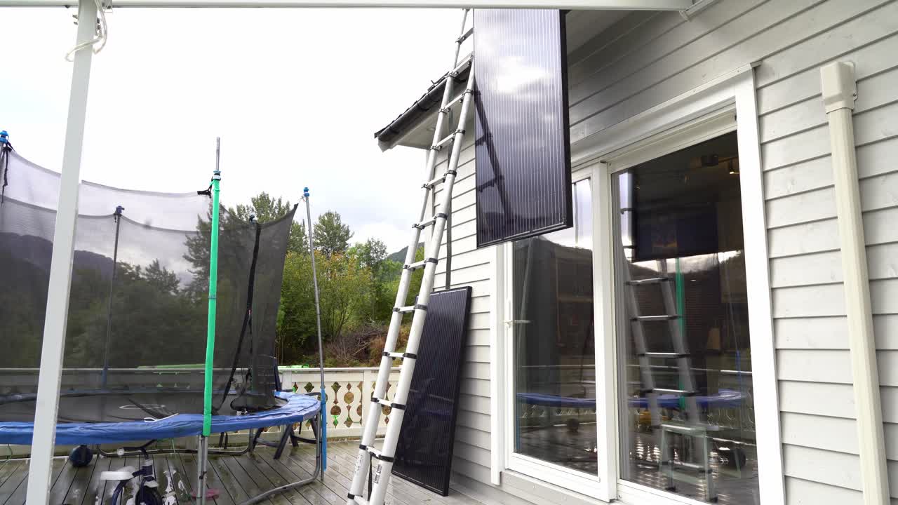 Solar panel lowered down from rooftop and homeowner climbing down ladder to release rope from panel - Removing solar panel installation from private house in Norway