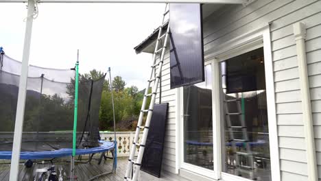 solar panel lowered down from rooftop and homeowner climbing down ladder to release rope from panel - removing solar panel installation from private house in norway
