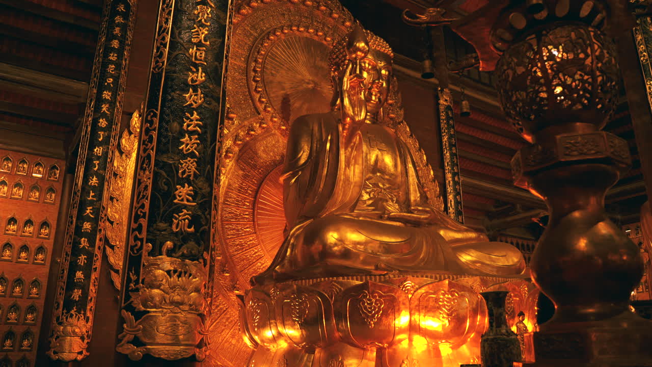 Una maestosa statua dorata di Buddha di grandi dimensioni seduta su un piedistallo a forma di loto all'interno del sontuoso interno in legno del complesso della Pagoda di Bai Dinh a Ninh Binh, Vietnam