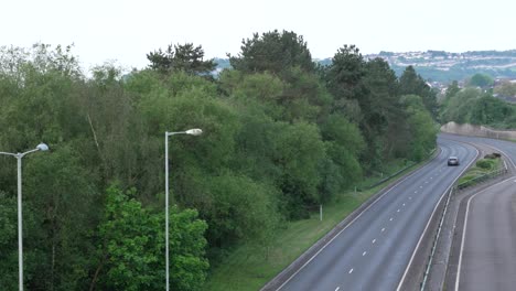 Einsames-Auto-Auf-Einer-Zweispurigen-Straße-Bei-Sonnenaufgang-Mit-Bäumen-Und-Straßenlaternen