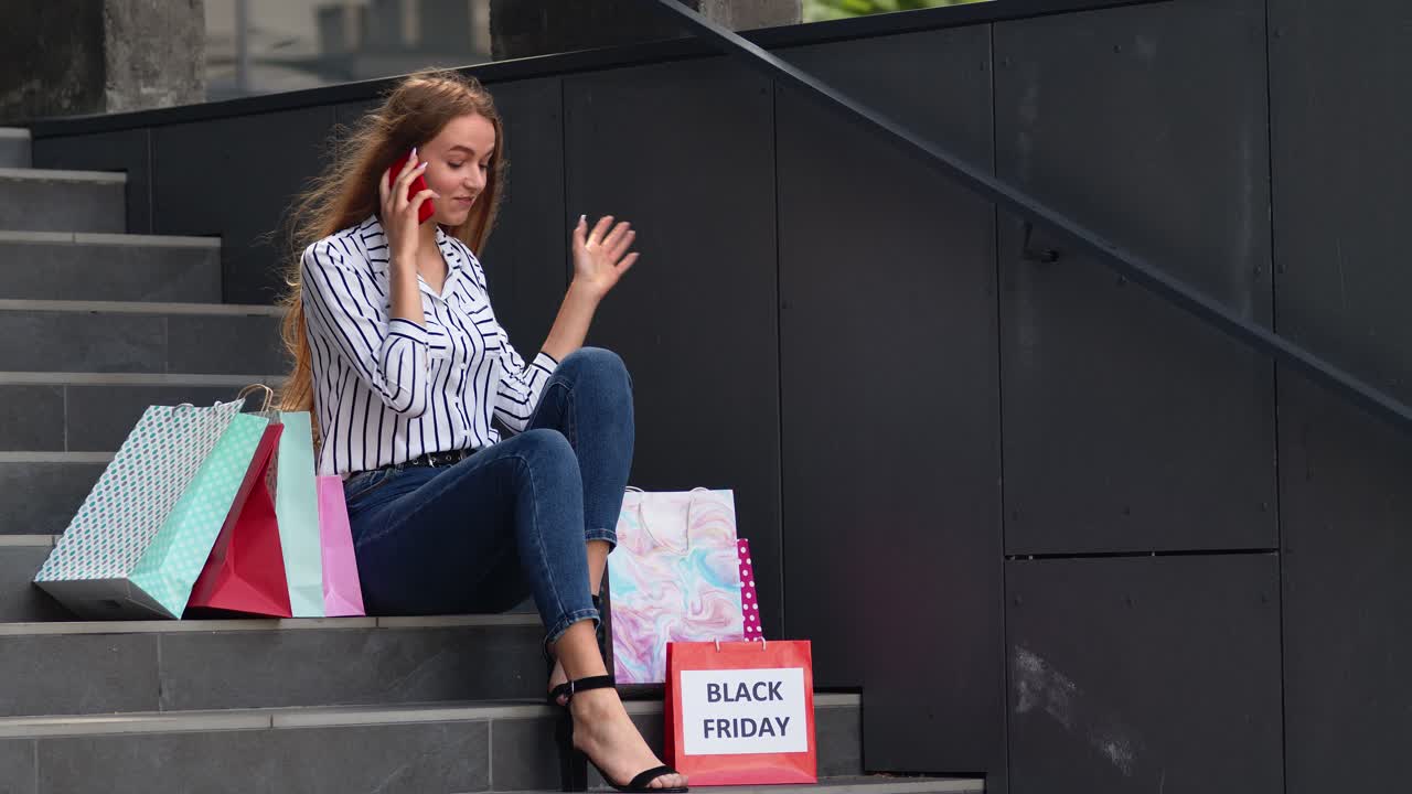 chica sentada en las escaleras con bolsas hablando en el teléfono móvil sobre la venta en el centro comercial en black friday