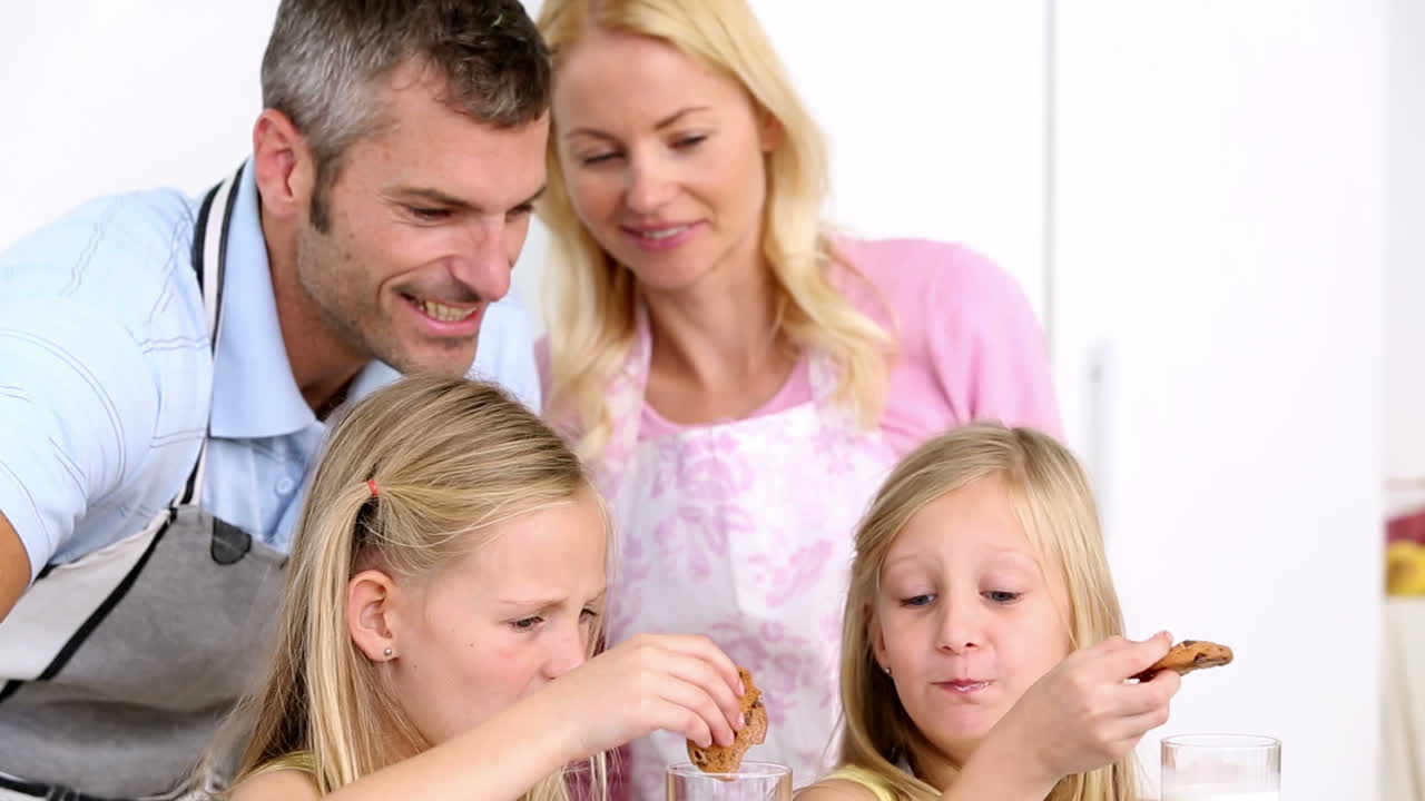 딸들이 부모와 함께 쿠키와 우유를 먹고 있습니다.