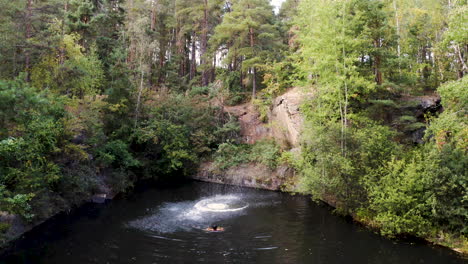 Man-jumping-into-a-forest-lake-from-a-cliff,friend-swimming,Czechia