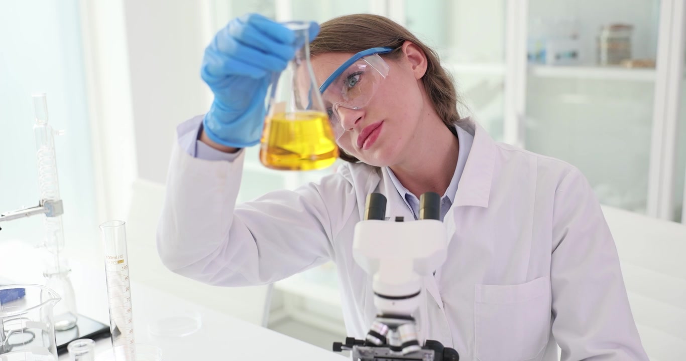 Scientist leans closer to beaker to observe yellow liquid